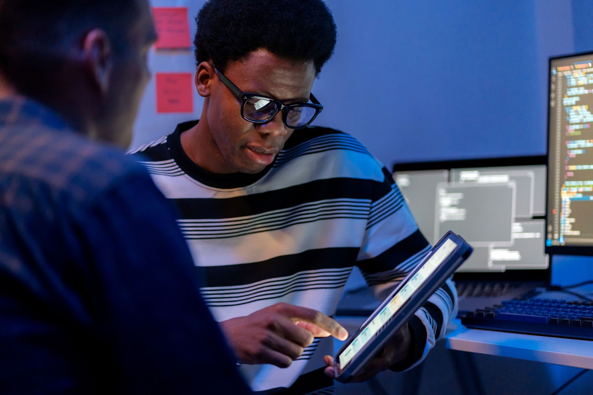 A multiracial software engineer leads a discussion on software development and testing processes in a modern tech business office. Using a digital tablet to display data, the engineer explains strategies to enhance the functionality and reliability.